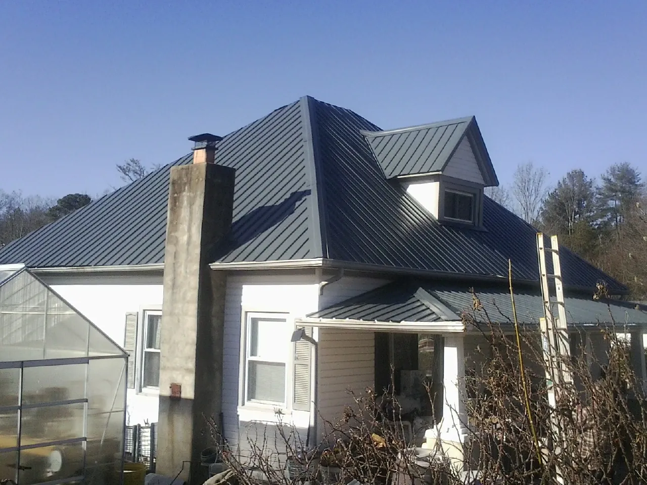 Dark blue standing seam metal roof on a white farmhouse with dormer — Slate & Tile Roof Repair by Roofing Brothers in Bigfork