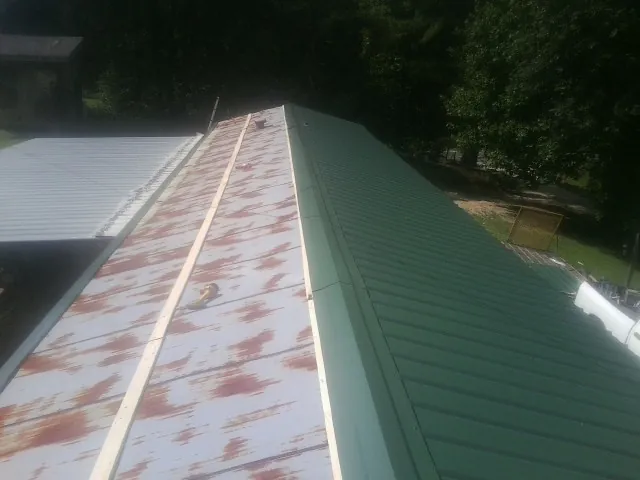Old rusted panels beside newly installed green metal roofing — Wind Damage Roof Repair by Roofing Brothers in Bigfork