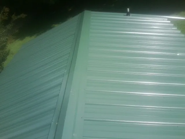 New green metal panels meeting at the ridge of a roof — Flat Roof Repair work by our crew in Bigfork