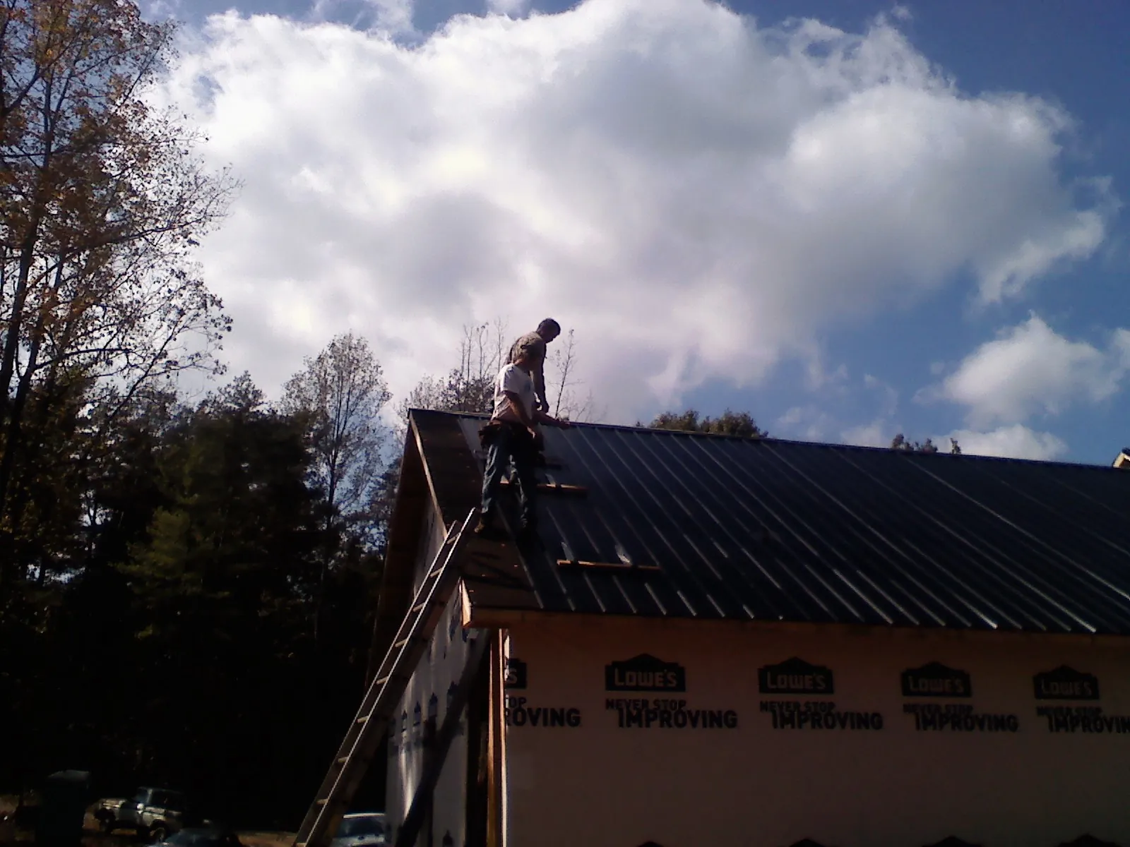 Roofer fastening dark metal panels high against a cloudy sky, from a Roof Inspection job in Bigfork