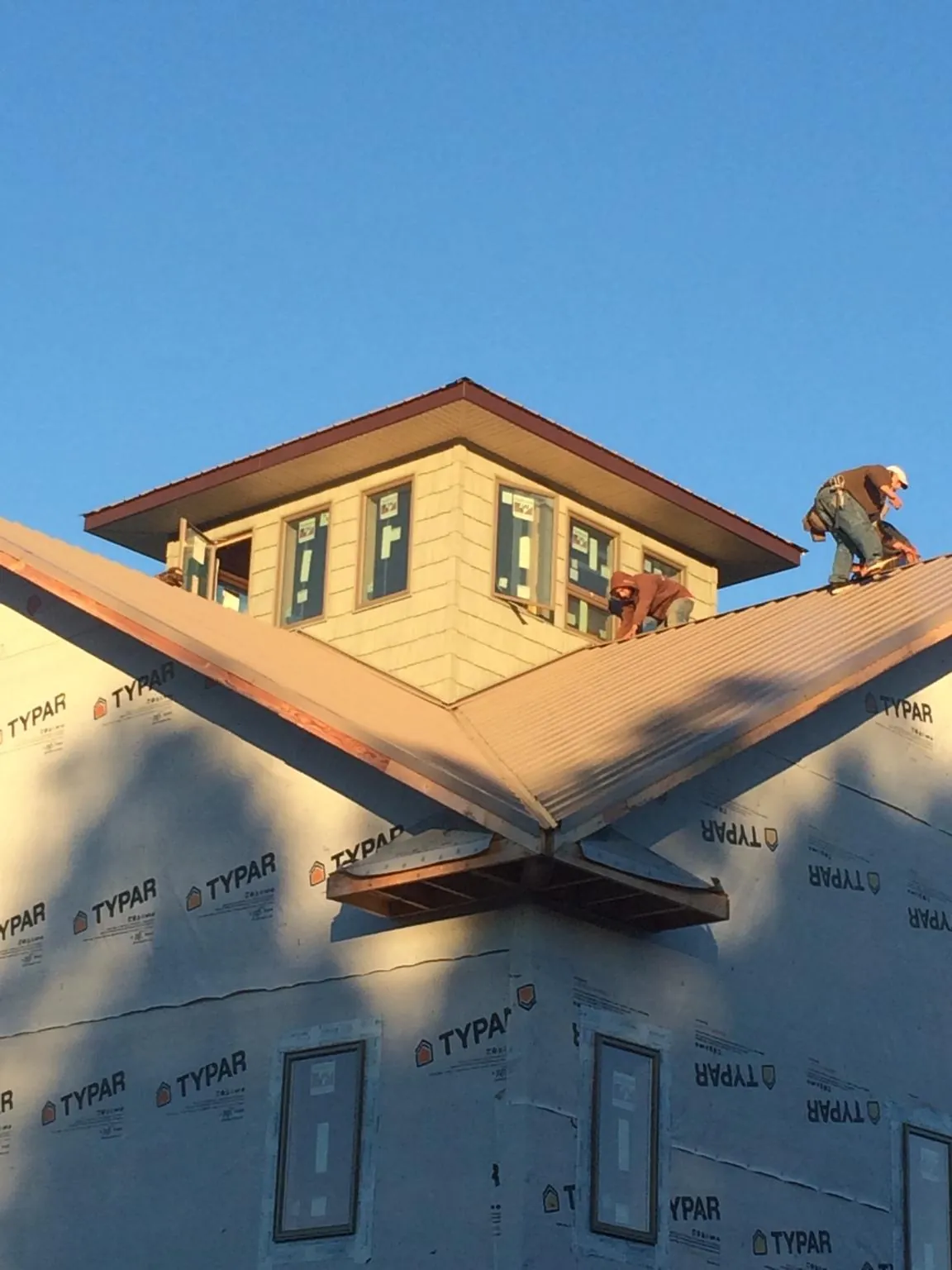 Roofers working around a rooftop cupola on a new metal roof at sunset — Roof Waterproofing in Bigfork by Roofing Brothers